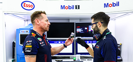 Max Verstappen and a Red Bull engineer talking in the RB garage with a Mobil 1 logo behind them