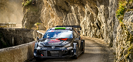 Toyota racing car driving down a gravel path with rocks above