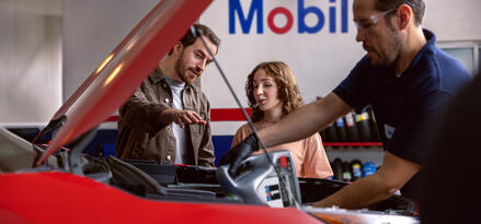 dad with daughter observing mechanic fill red car with Mobil oil