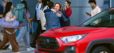 Couple embracing goodbye at the airport with red car