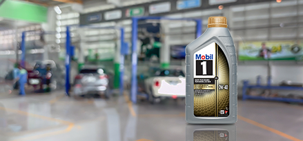 Bottle of Mobil 1 0W-40 motor oil in a blurred car repair shop.
